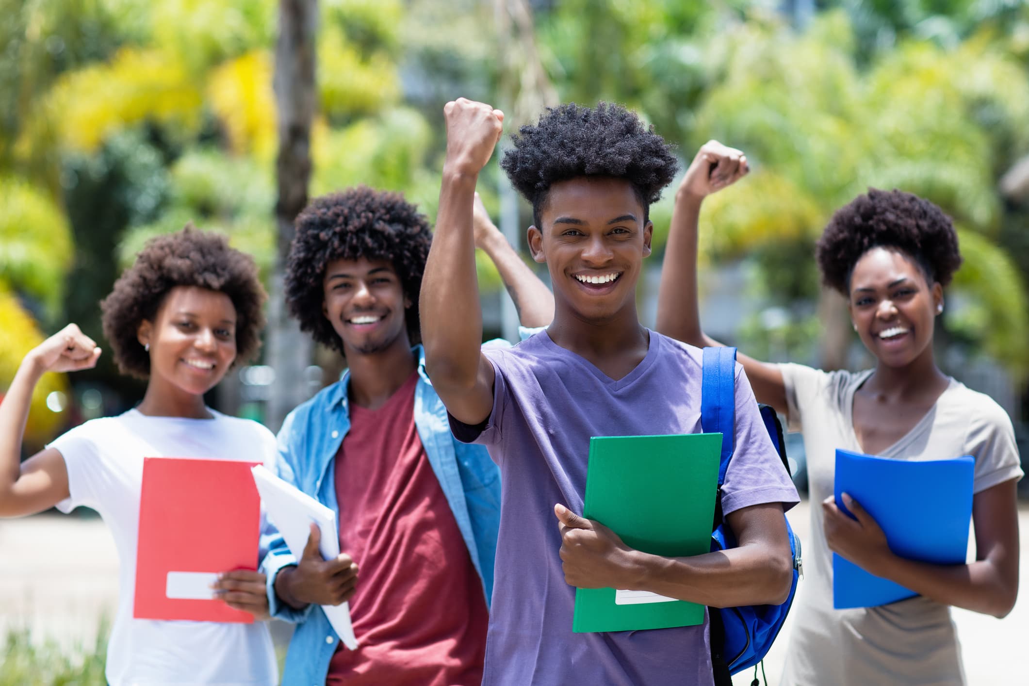 Four young people smiling with arms raised in celebration, holding folders